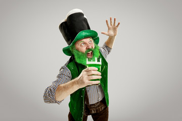 A smiling happy senior man in a leprechaun hat with green beer at studio. He celebrates St....
