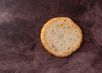 Top view of a single sesame round melba toast on a maroon background.