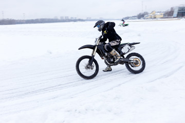 Biker motorcyclist riding on snow and ice in cold winter day. Extreme winter sport. 