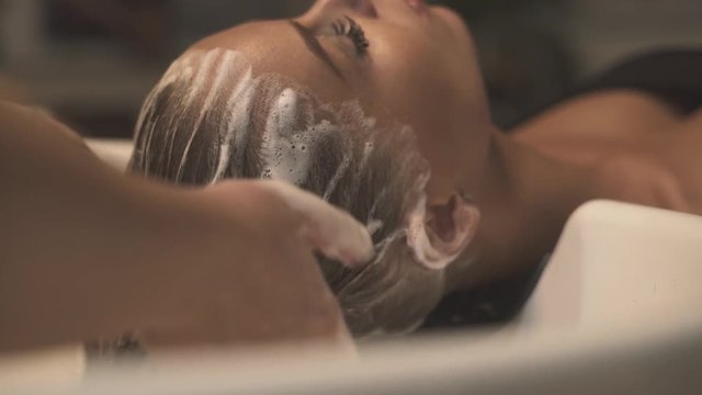 Hairdresser washing female hair and head in beauty studio before haircut. Close up hairstylist washing head with massage in hairdressing salon. Young woman in beauty salon. Treatment and spa care.