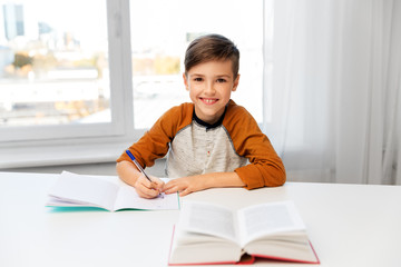 education, childhood and people concept - happy boy doing homework and writing to notebook at home