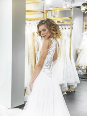 Woman choosing wedding dress in shop. Attractive young bride is smiling while choosing wedding dress in modern wedding salon. Future wife. Woman surrounded by wedding dresses.