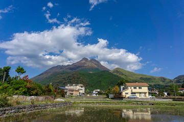 Obraz premium Beautiful lanscape panorama of Yufuin village and Yufu mountain in Background with blue sky and clouds in autumn leaves. onsen town, Yufuin, Oita, Kyushu, Japan