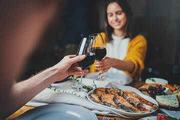 Romantic couple enjoying date night in restaurant, cozy atmosphere, Love Relationship Dinner Concept, sweet couple making cheers with glasses of red wine during romantic evening