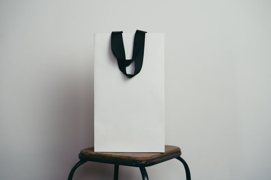 Mock-up of blank package, mockup of white paper shopping bag with handles on wooden chair on the white background, empty area with copy space for your logo or design
