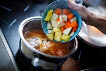 the shredded vegetables pouring into the boiling goulash soup in pot