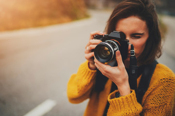 Young female photographer taking photograph on vintage camera outdoors, blank space for text message or design, tourist girl enjoying road trip in Europe, flare light - obrazy, fototapety, plakaty