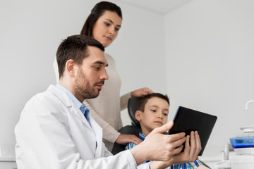Obraz premium medicine, dentistry and healthcare concept - dentist showing tablet pc computer to kid patient and his mother at dental clinic