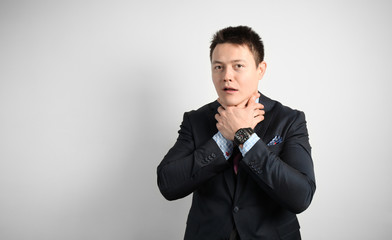 Young businessman in suit on gray background choking himself with his hands. Crash at work, taxes.