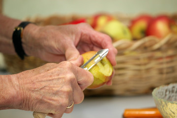 Senioren Hand von alter Frau sch&auml;lt und schneidet Apfel. Im Hintergrund ist Kotb mit &Auml;fpeln.