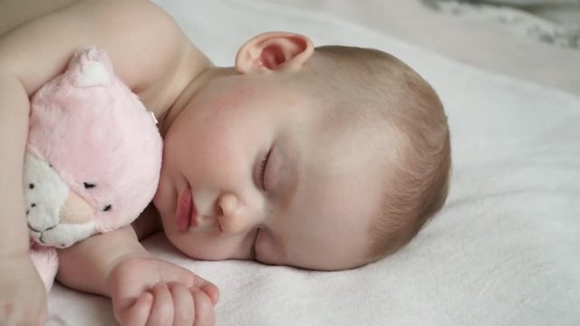 Close-up of a cute newborn baby girl sleeping with a soft pink cat toy