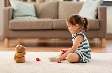 childhood and people concept - happy three years old baby girl playing tea party with toy crockery and teddy bear at home