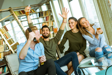 Group of young friends looking at the TV, drinking cider and having fun  in the room