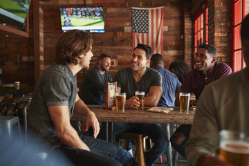 Group Of Male Friends Meeting And Drinking Beer In Sports Bar Together
