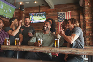 Group Of Friends Watching Game On Screen In Sports Bar - obrazy, fototapety, plakaty
