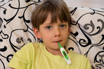 Sick boy with thermometer in his mouth laying in bed. Sick child with fever and illness in bed. Checking temperature. - Image