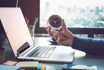Business concepts with businessman holding clock on computer laptop.For investment analysis,Waiting to sucess - obrazy, fototapety, plakaty