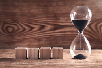 Hourglass with wooden cubes on wooden background.
