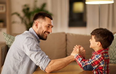 Fototapeta premium family, fatherhood and people concept - happy smiling father and little son arm wrestling at home in evening