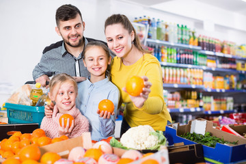 Happy family with two little girls looking for fresh oranges in supermarket