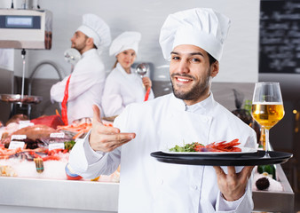 Portrait of professional chef with serving tray offering seafood in fish restaurant