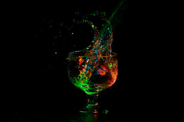 Liquid splashing out from glass with stem with vibrant colored lights on black