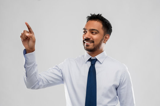 business, office worker and people concept - smiling indian businessman touching something invisible or working with virtual screen over grey background