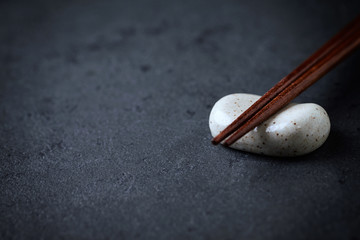 Wooden chopsticks and chopstick rest on black stone background. Close up. Copy space. 