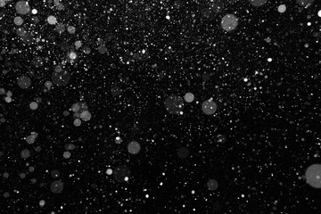 Real snow falling on black background. Falling snow of different shapes and sizes. Blurred snow...