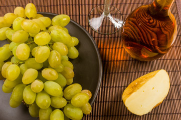 large brush of green grapes in a ceramic plate, a decanter and a glass of wine and cheese