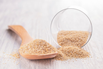 Oat bran in a wooden spoon and in a glass transparent glass on a white wooden table