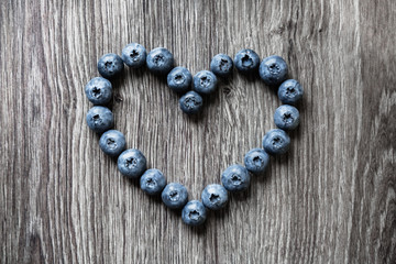 Ripe tasty blueberries and berries on a wooden table in the shape of heart