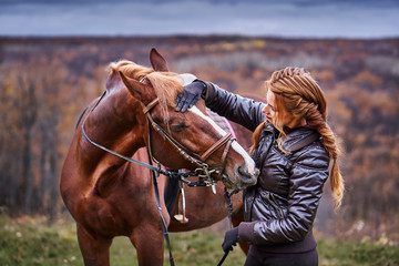Obraz premium a young woman with brown hair gently communicates with her beloved horse. Autumn cloudy day.