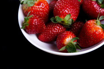 Strawberry in white plate close up on dark background