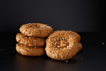 A bunch of homemade oatmeal cookies with nuts, chocolate chips and sesame. On a black background.