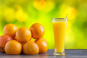 Tall glass of tasty freshly squeezed orange juice standing on an outdoor table with a fresh oranges