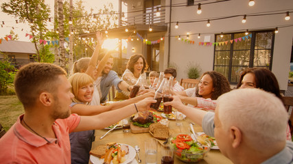 Family and Friends Gathered Together at the Table Raise Glasses and Bottles To Make a Toast and...