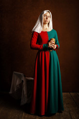 Portrait of a beautiful girl in a medieval dress in red and green on a brown background.