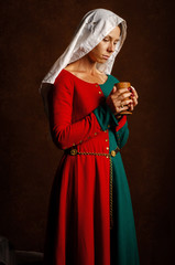 Portrait of a beautiful girl in a medieval dress in red and green on a brown background.