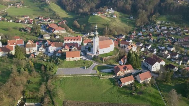 Aerial: Flying over catholic church with big parking place beside. Filming small village on beautiful spring sunny day.