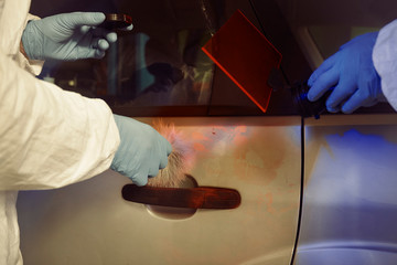Crime investigation - developing of fingerprints on suspected car in police garage under UV light