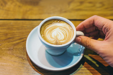 First morning coffee in cafe. Hand holding coffee cup on the wooden table, heart shape