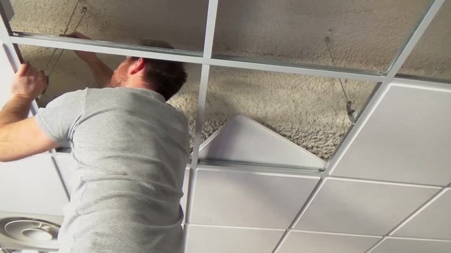 Construction worker assemble a suspended ceiling with drywall and fixing the drywall to the ceiling metal frame with screwdriver.
