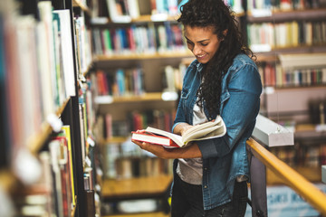 Young female student read and learns by the book shelf at the library.Reading a book.