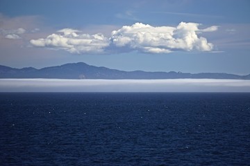 Fototapeta premium Morning at sea: Clouds and fog over Alaskan islands in the North Pacific Ocean.