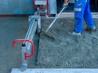 Worker on a laser screed machine leveling fresh poured concrete surface on a construction site