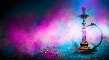 Smoking hookah on the background of an empty room. Multicolored neon light. Searchlight, laser blue and pink rays, smoke.