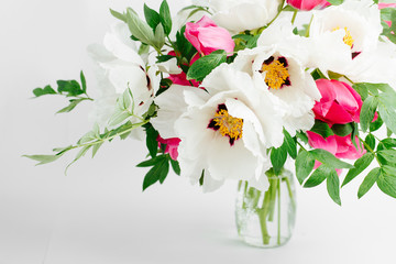 Beautiful bouquet of white peonies and pink tulips in a glass vase on a white background