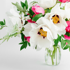 Beautiful bouquet of white peonies and pink tulips in a glass vase on a white background