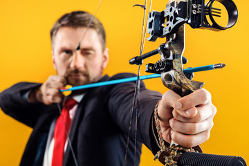 Businessman aiming at target with bow and arrow, isolated on yellow studio background. The...
